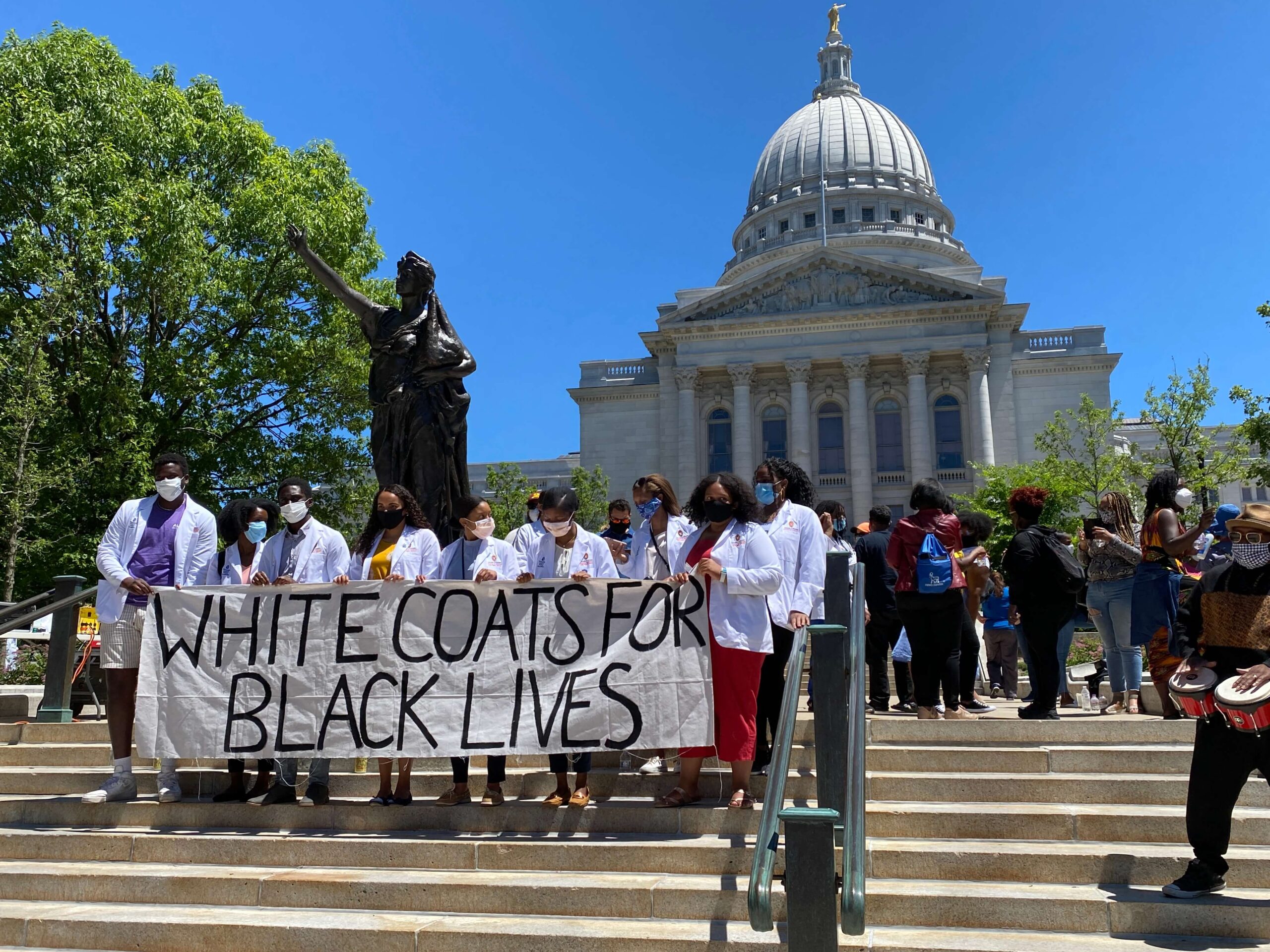 students holding up banner reading "White Coats for Black Lives" in front of capitol building