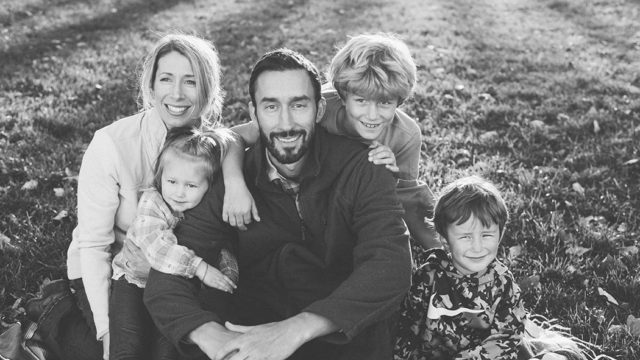 Alum Nate Johnson sits in the grass with his wife and three children.