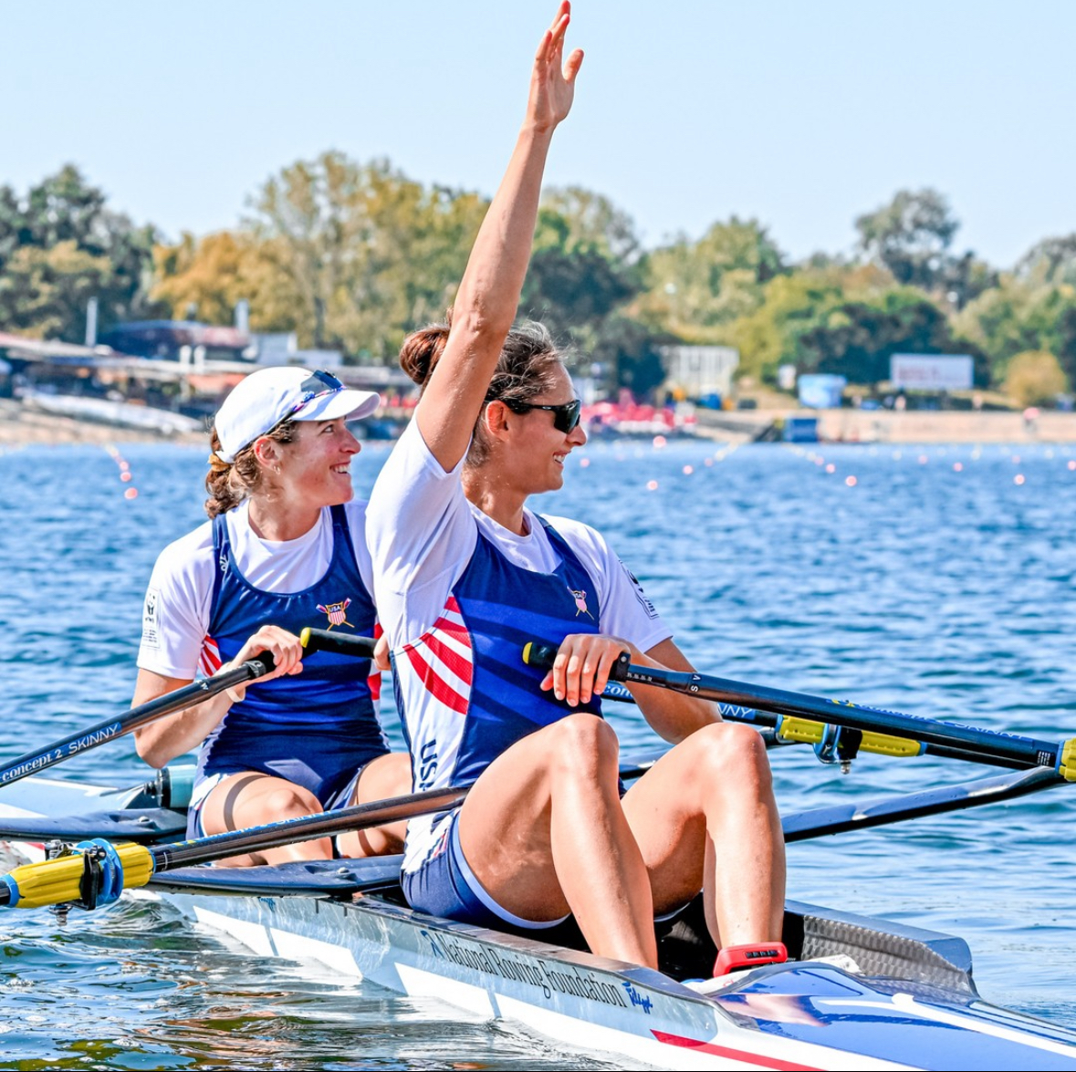 Sophia Vitas sits in a scull, with one arm up and the other holding a paddle.