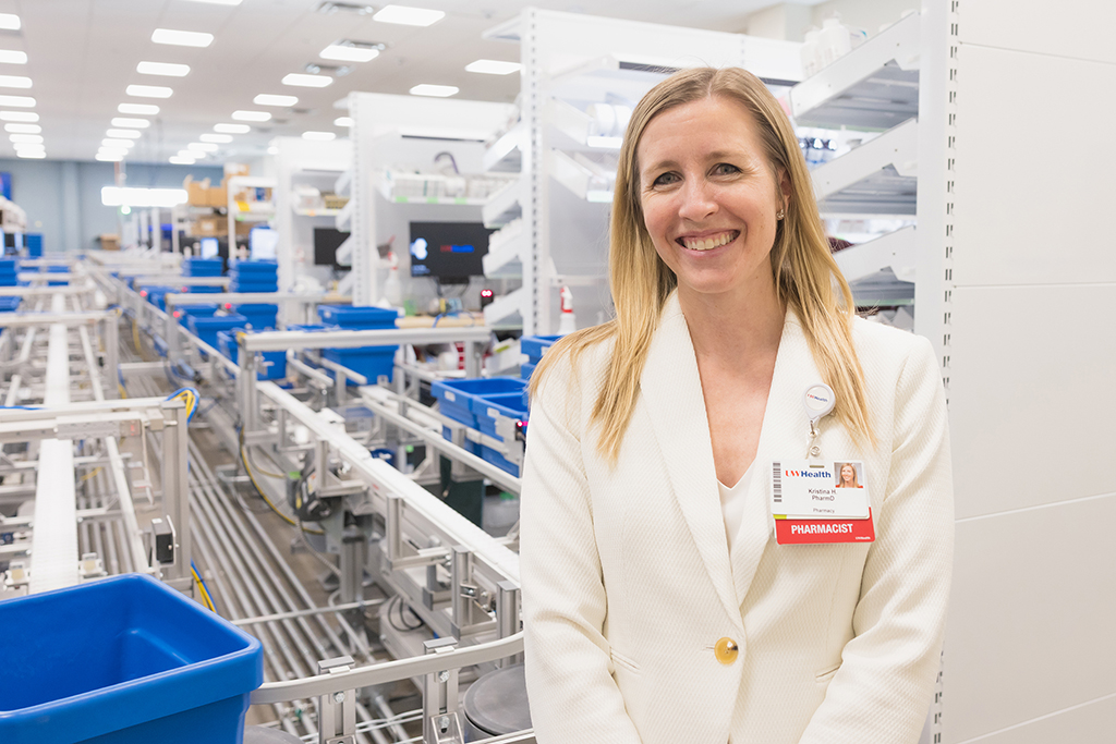 Kristina Heimerl poses in a white blazer in front of a pharmacy preparation area