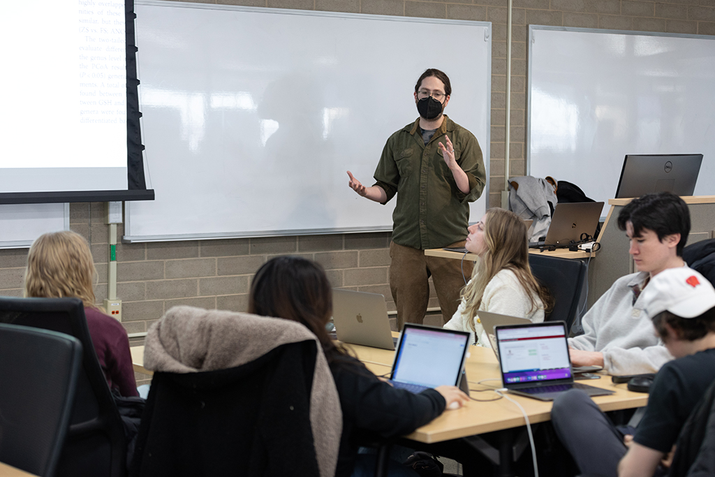 A graduate student gesturing in front of a class of students.