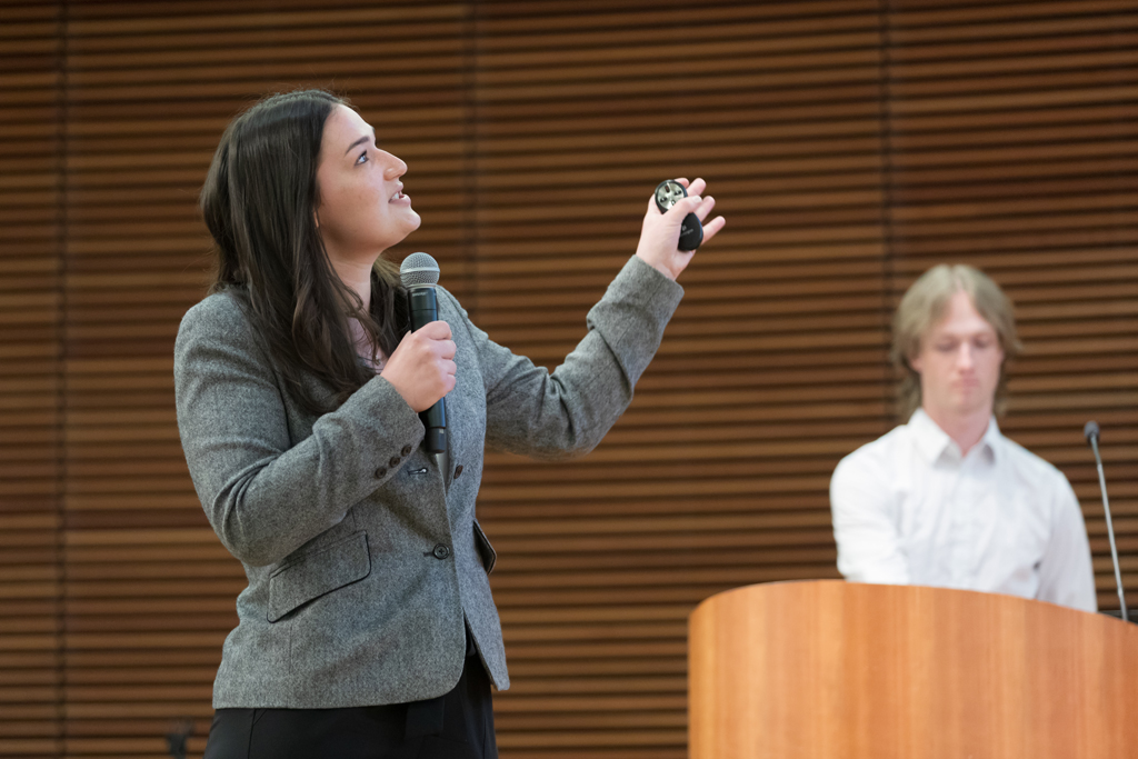 A PharmD student gestures to the left while speaking into a microphone