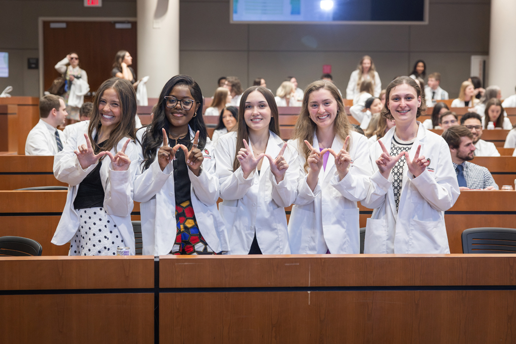 SoP Pinning Ceremony 2026 Pharmacy students in white coats holding up their hands in a W shape