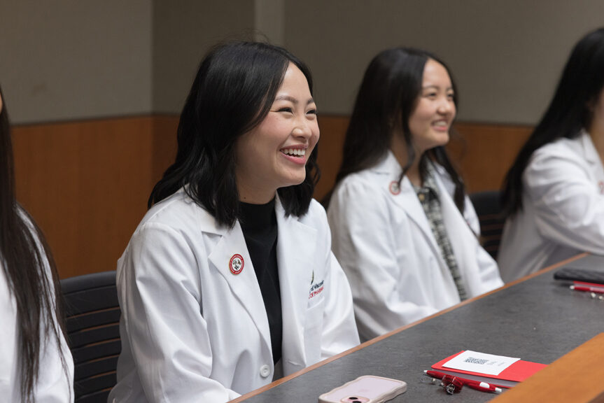 Female PharmD students smiling while seated in their white coats