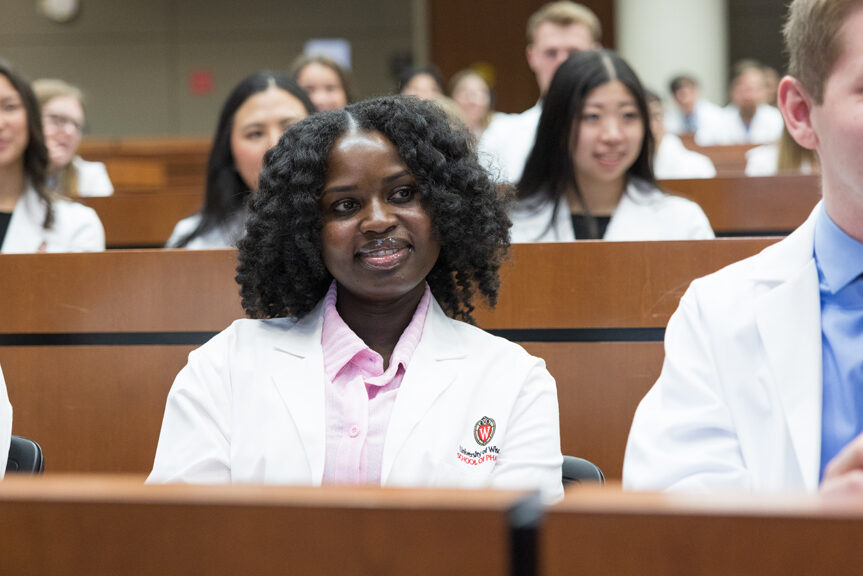 PharmD students in their white coats smile while seated in a a lecture hall