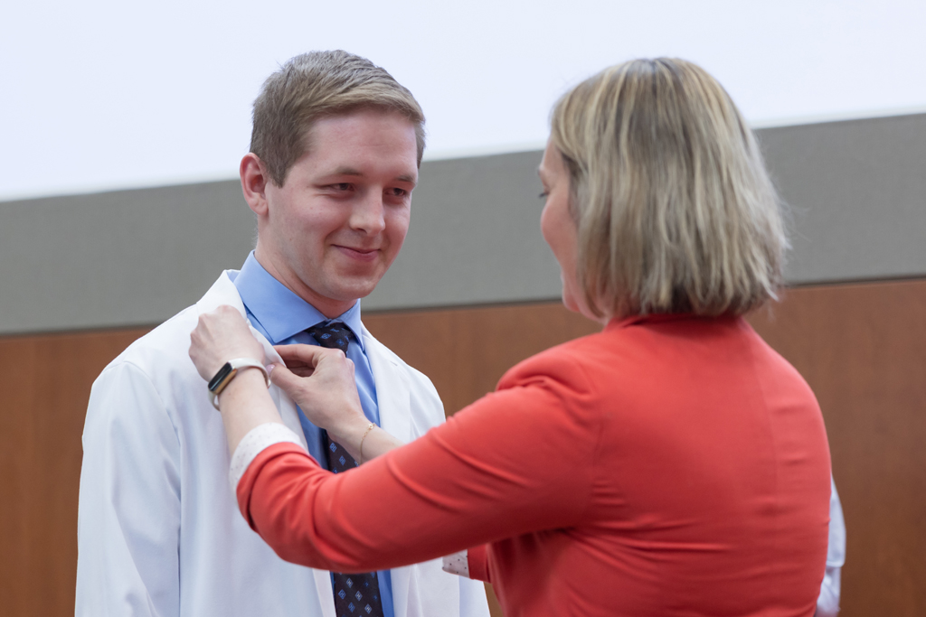 A PharmD student receives a pin on the lapel of their white coat