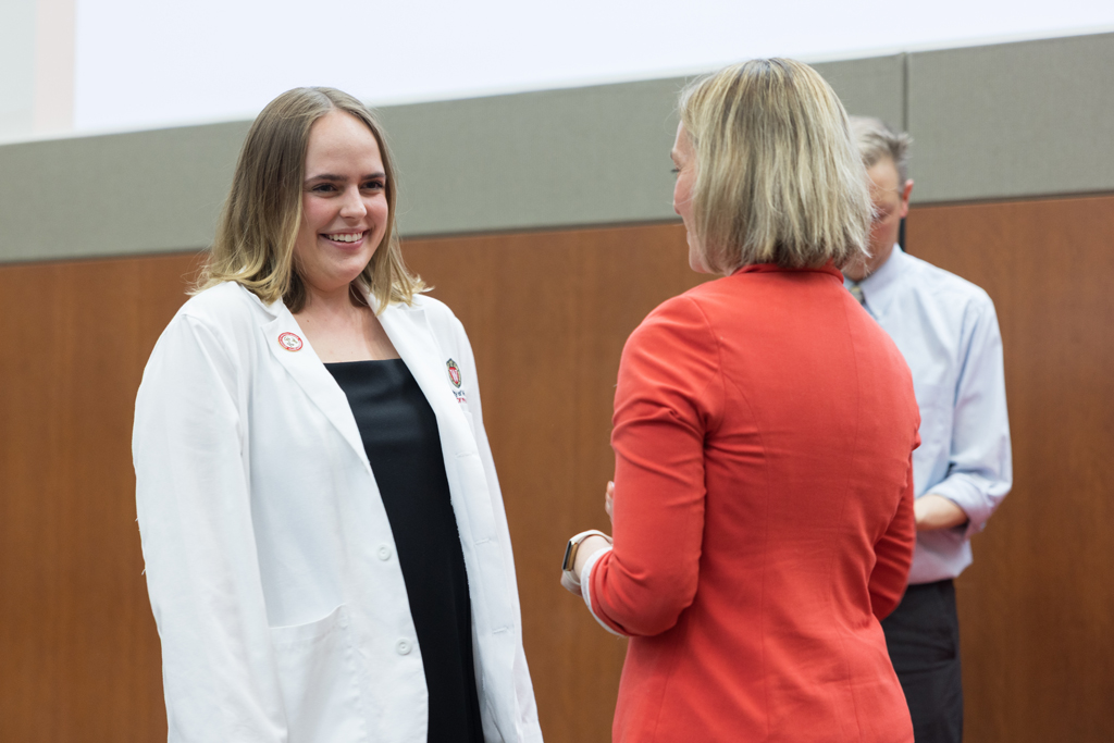 A PharmD student receives a pin on the lapel of their white coat