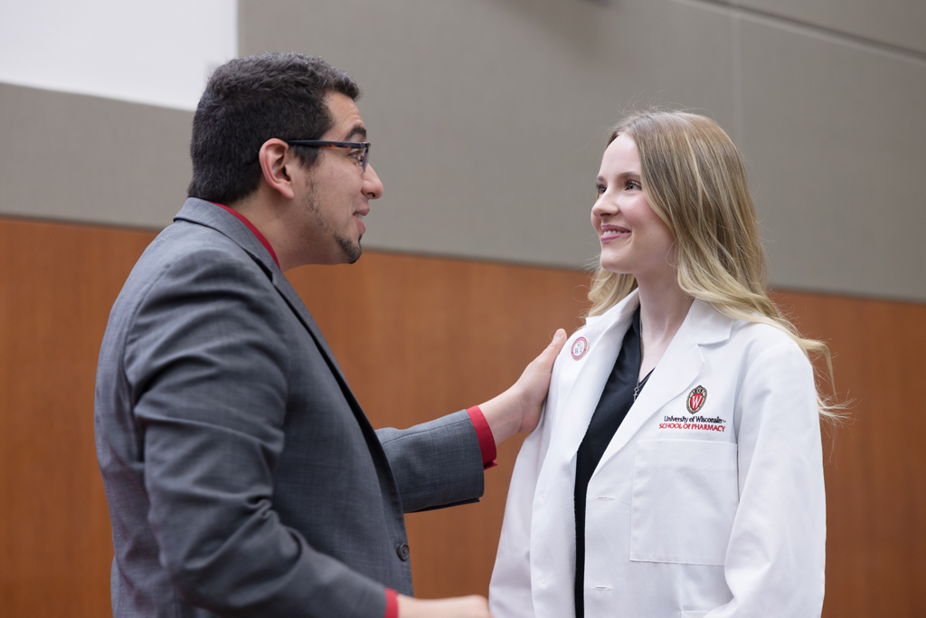 A PharmD student receives a pin on the lapel of their white coat