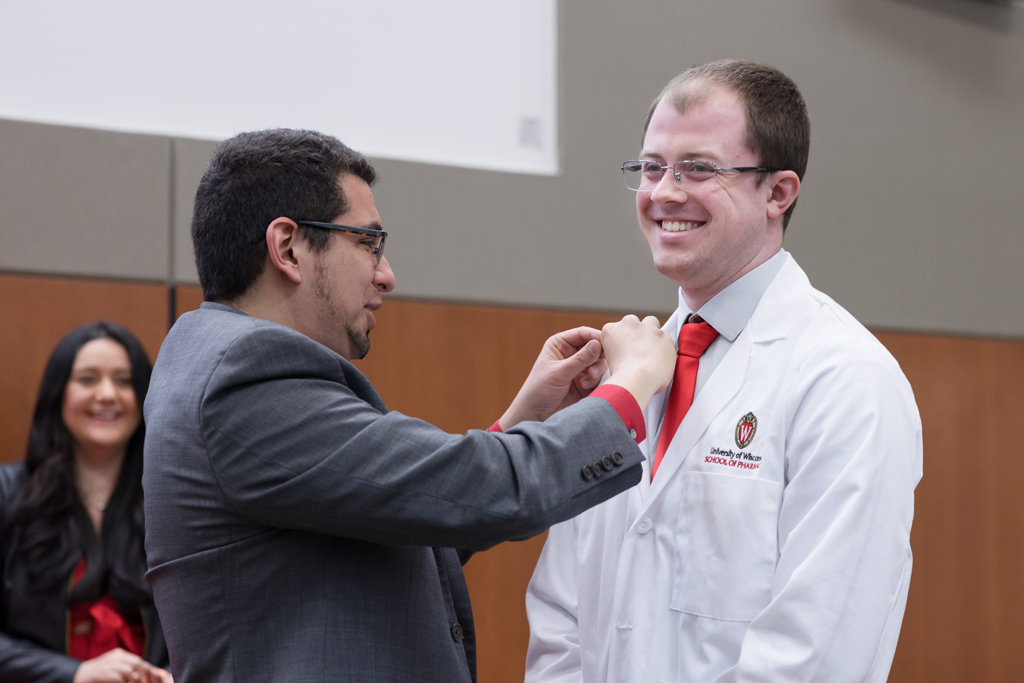 A PharmD student receives a pin on the lapel of their white coat