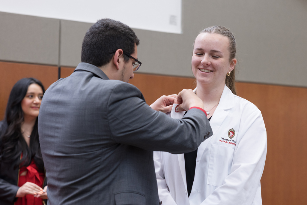 A PharmD student receives a pin on the lapel of their white coat