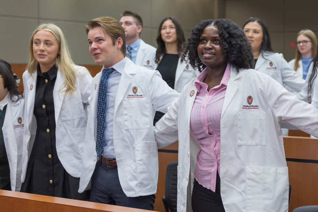 Arm in arm, PharmD students in white coats sing