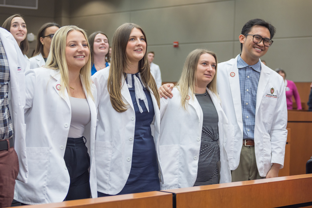 Arm in arm, PharmD students in white coats sing