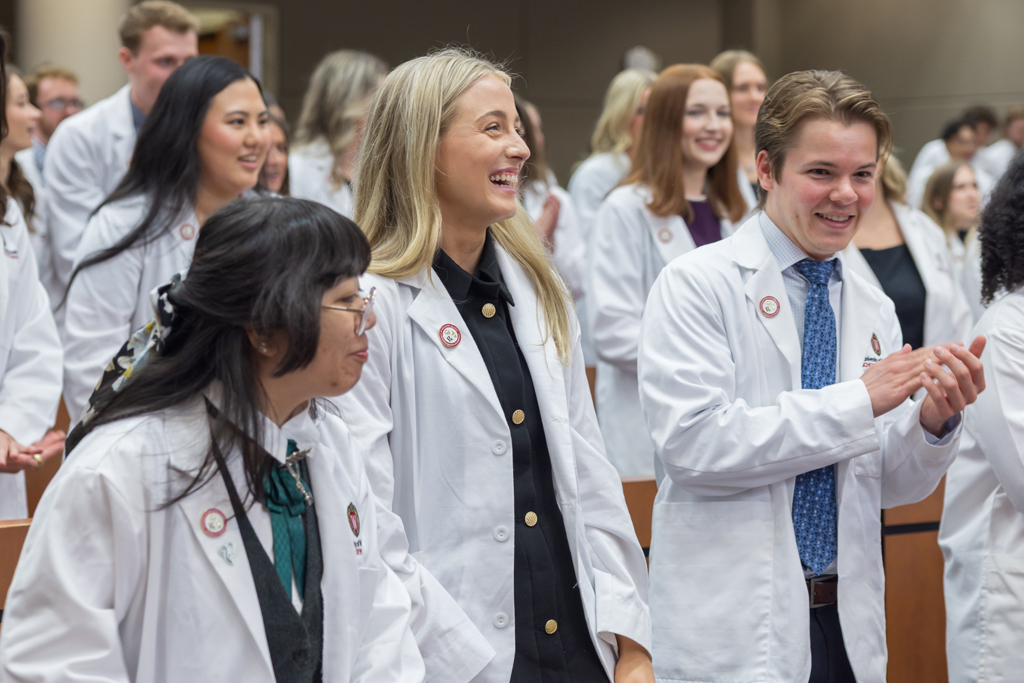 PharmD students in white coats laugh and clap