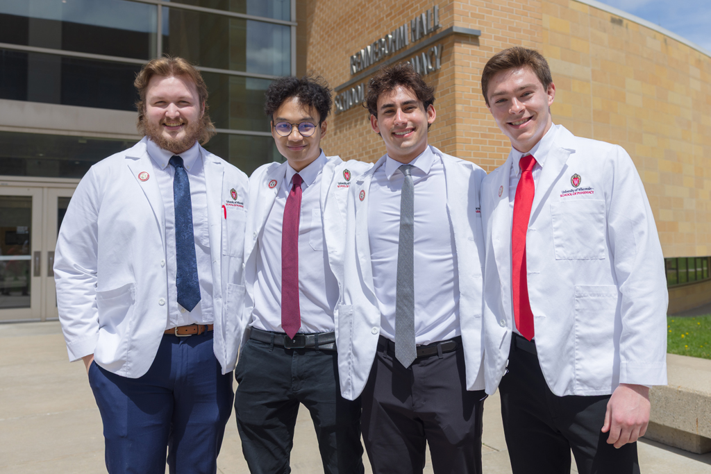 A group of PharmD students pose in front of Rennebohm Hall in their white coats