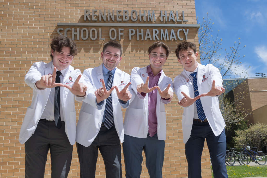 A group of PharmD students pose in front of Rennebohm Hall in their white coats