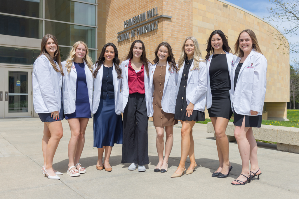A group of PharmD students pose in front of Rennebohm Hall in their white coats