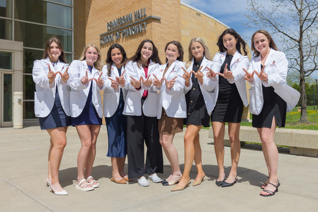 A group of PharmD students pose in front of Rennebohm Hall in their white coats