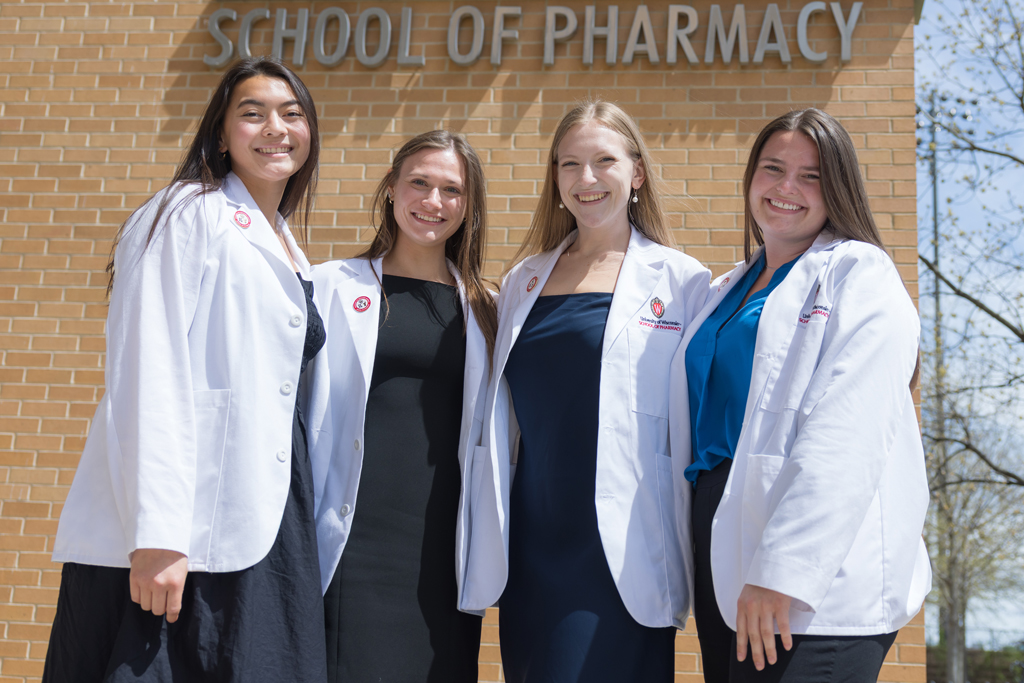 A group of PharmD students pose in front of Rennebohm Hall in their white coats