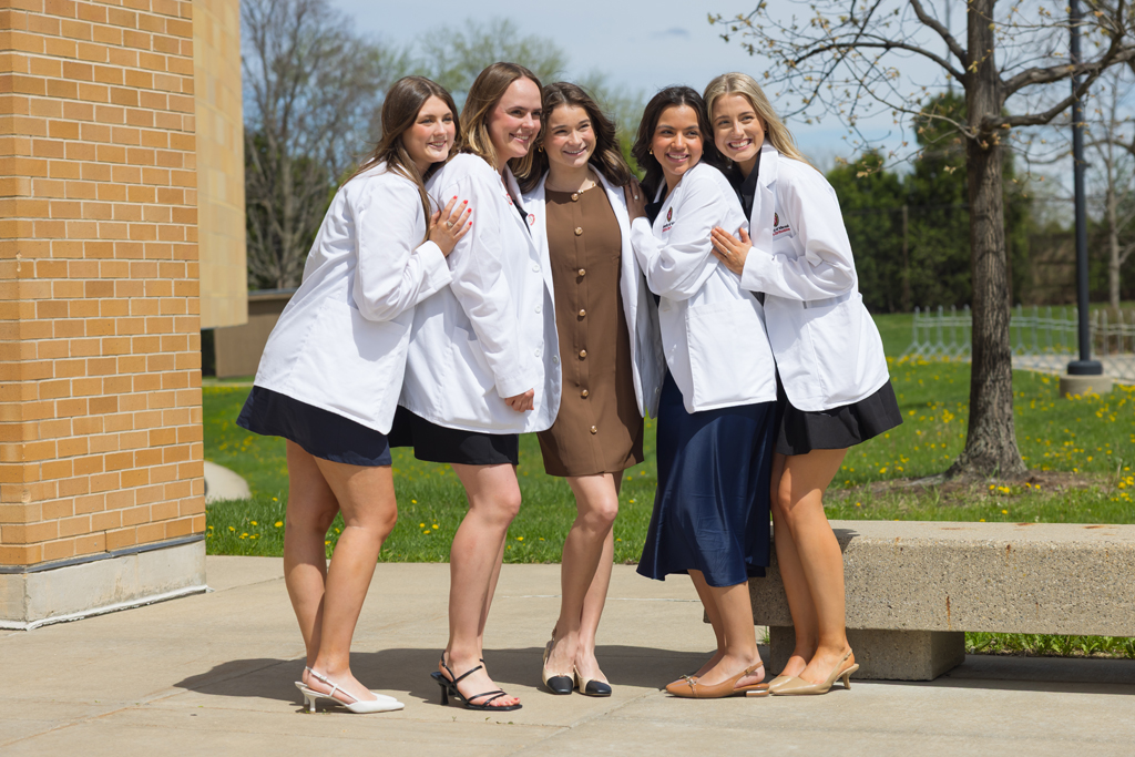 A group of PharmD students pose in front of Rennebohm Hall in their white coats