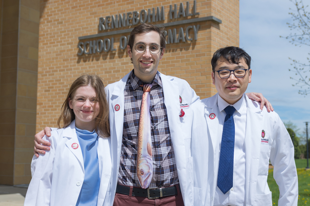 A group of PharmD students pose in front of Rennebohm Hall in their white coats