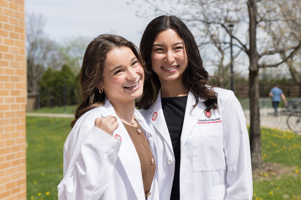 A group of PharmD students pose in front of Rennebohm Hall in their white coats
