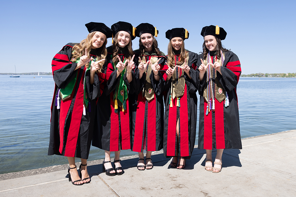 A group of graduates in robes hold up W hands