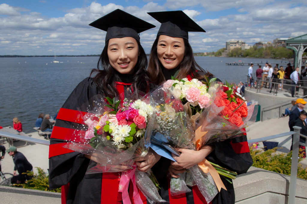 Two graduated students holding large bouquets together