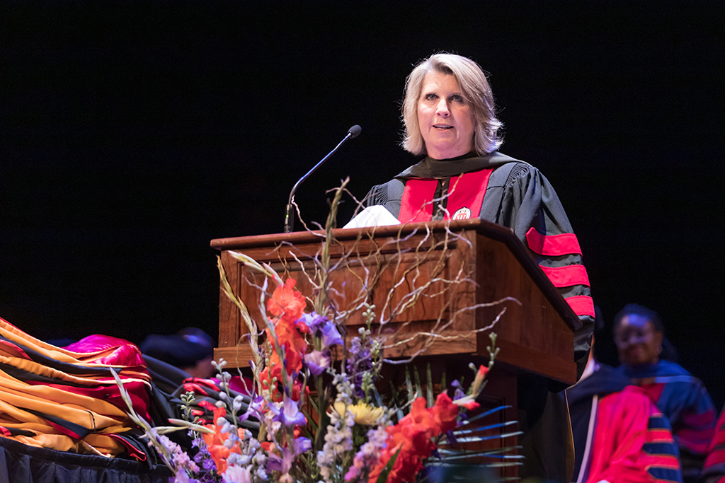Debra Fluno in graduation robes speaking at a podium