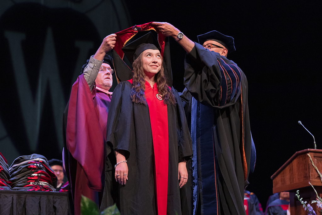 Faculty place a hood over a graduate's head.