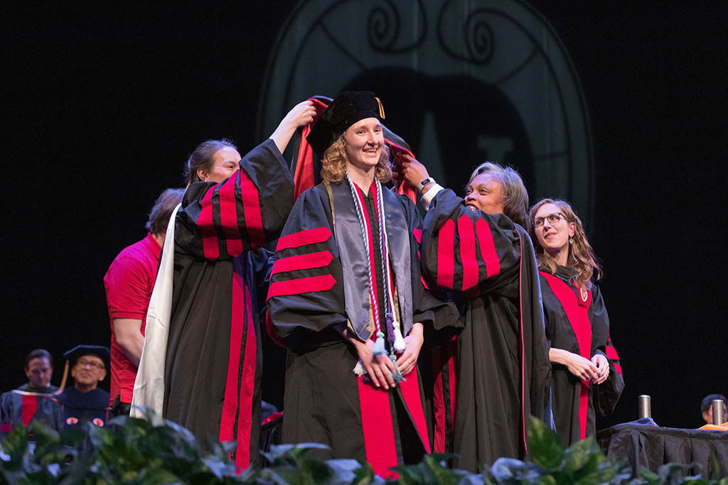 Faculty place a hood over a graduate's head.