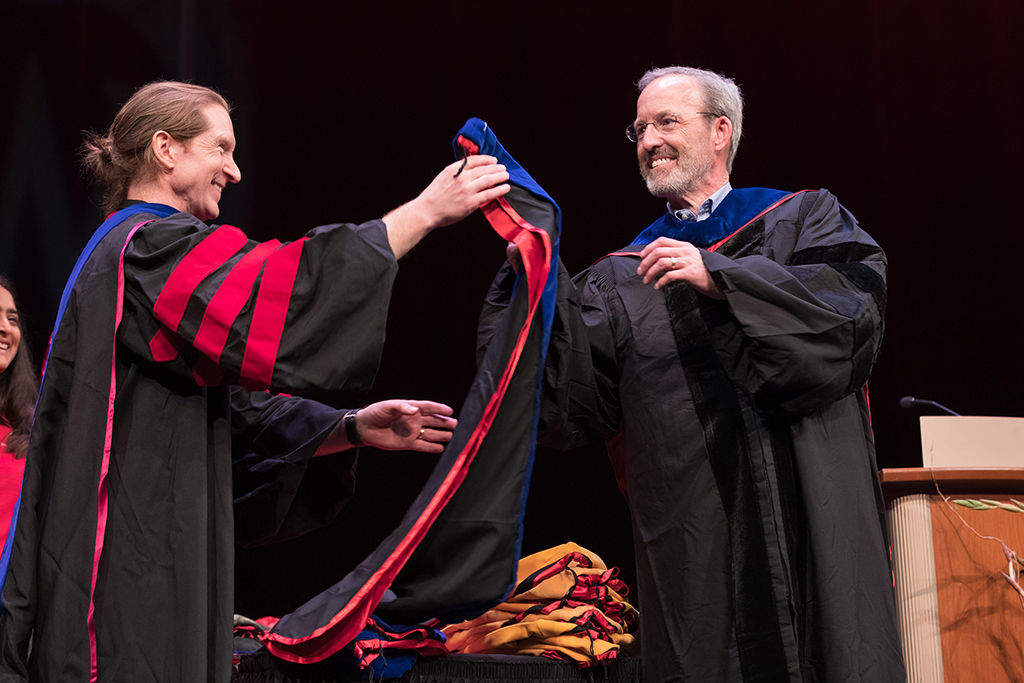 Dave Mott receiving a hood to bestow upon a student from a professor