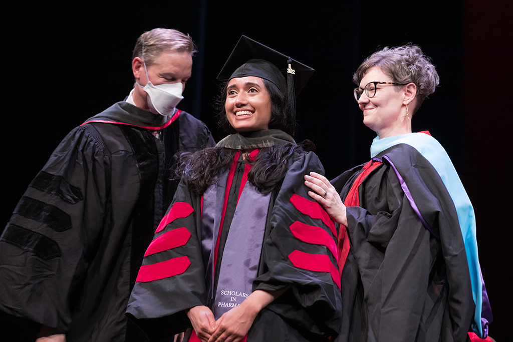 Two pharmacy professors bestowing a hood upon a graduate student at the hooding ceremony