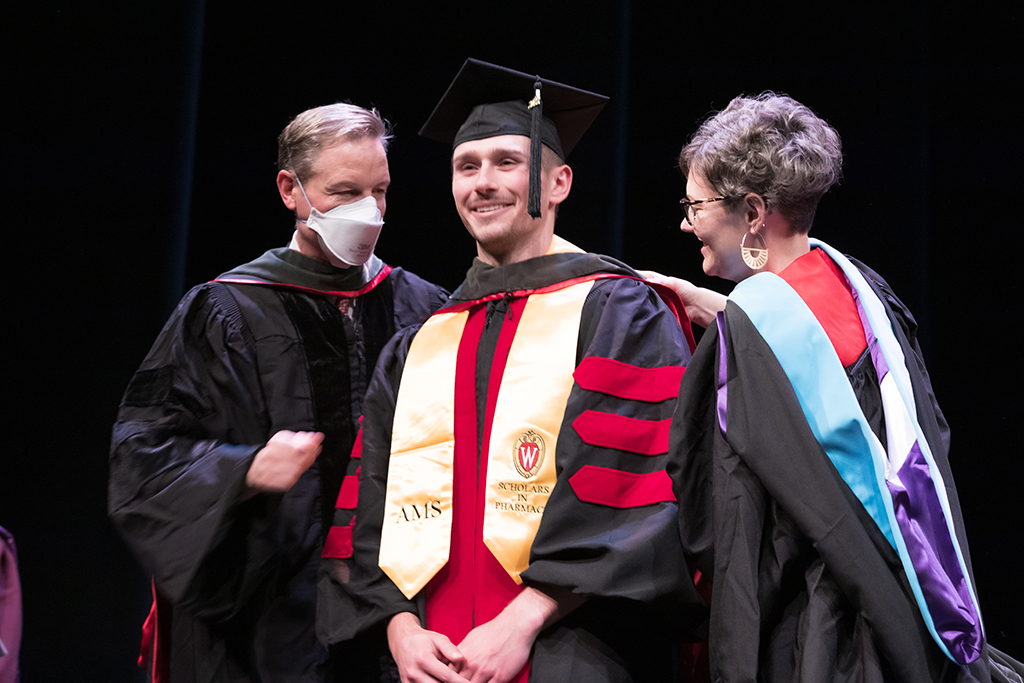 Class of 2022 PharmD graduate Logan Erdmann receives his hood from Professor John Dopp and Advisor Rebecca Beebe