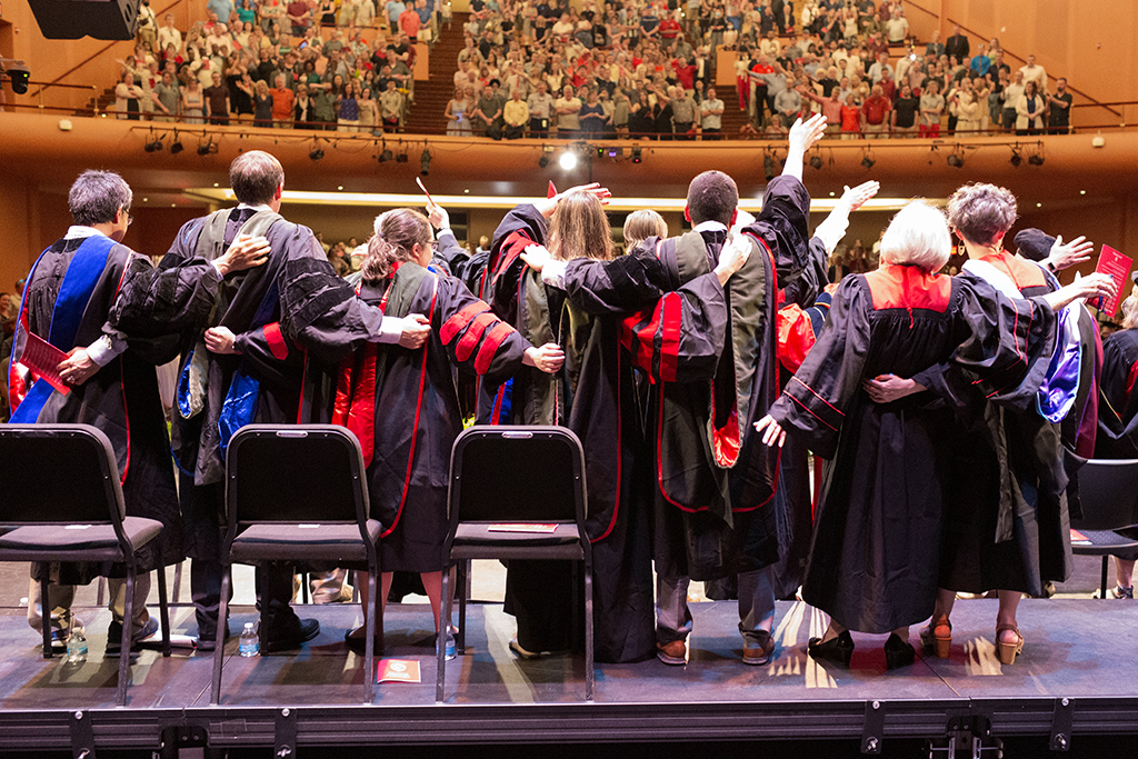 School of Pharmacy faculty and staff stand on stage singing Varsity at the conclusion of the 2022 Hooding Ceremony