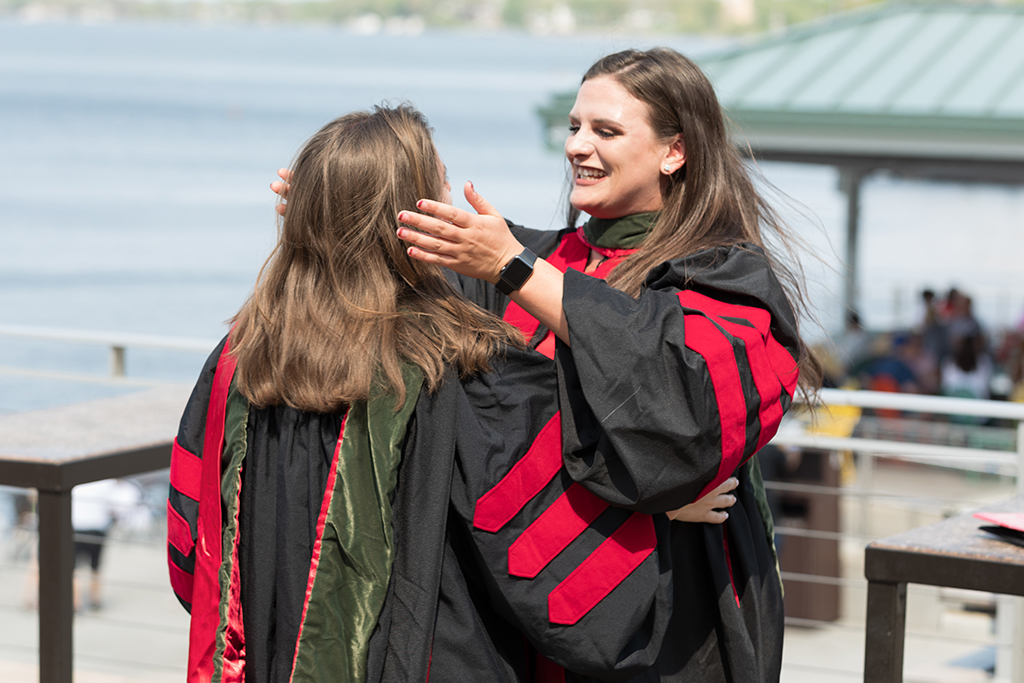 Class of 2022 PharmD graduate Lauren Streets heads into an embrace with a classmate at Memorial Union Terrace after the Hooding Ceremony