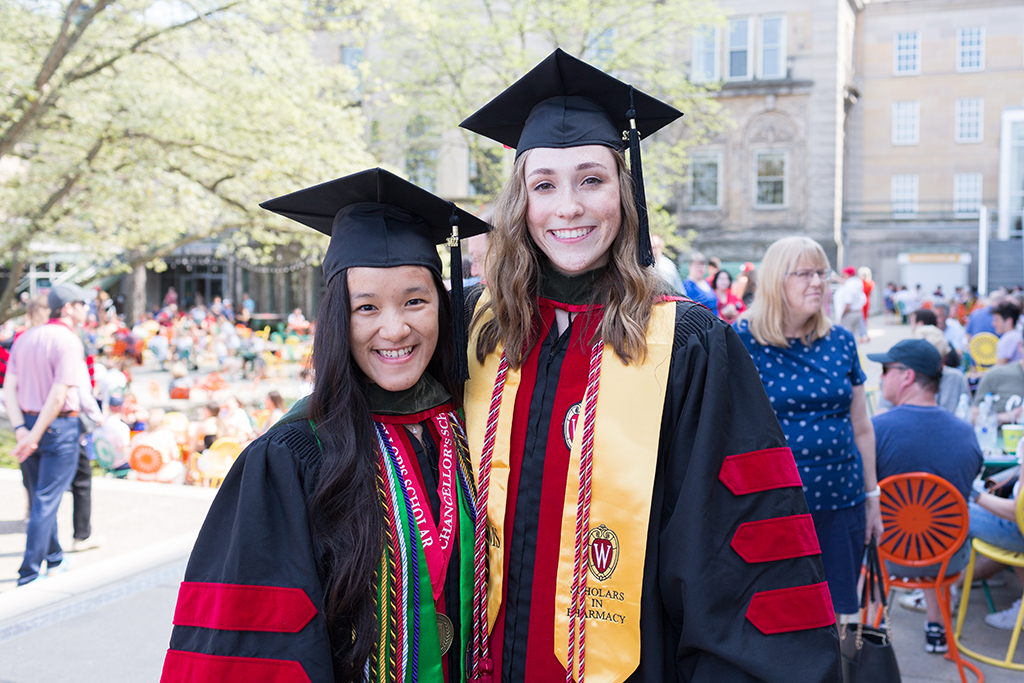 PharmD Class of 2022 grads Stepheaney Cheng and Emily Willey pose together in their cap and gowns at Memorial Union Terrace following the Hooding Ceremony.