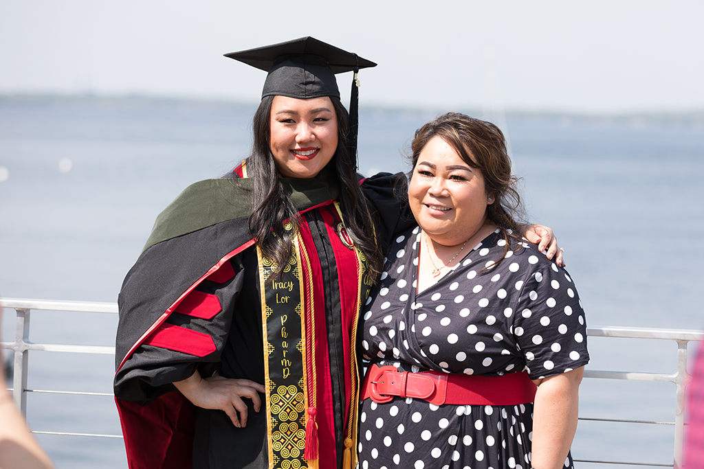 Tracy Lor poses in her cap and gown next to her mother next to Lake Mendora after the 2022 School of Pharmacy Hooding Ceremony