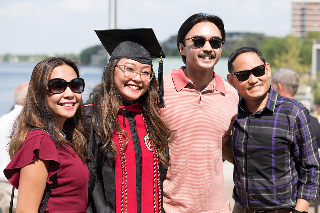 Pharmacy student Lorewell Buaya poses in her cap and gown with her family by Lake Mendota