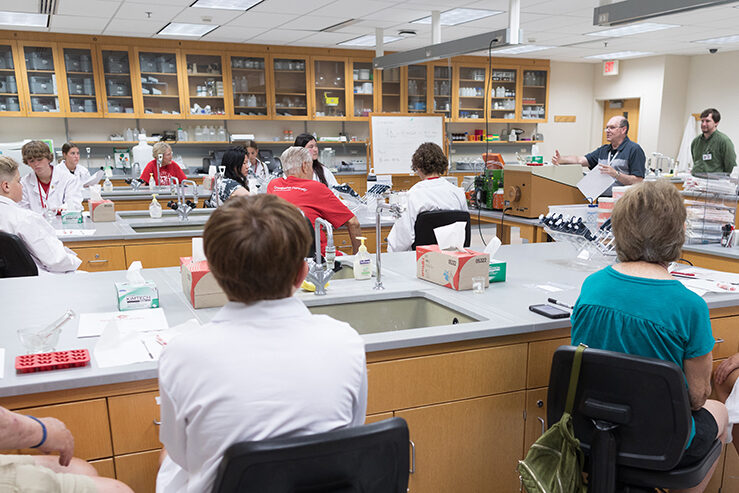 A group of attendees in a lab watch Ed Elder explaining the activity