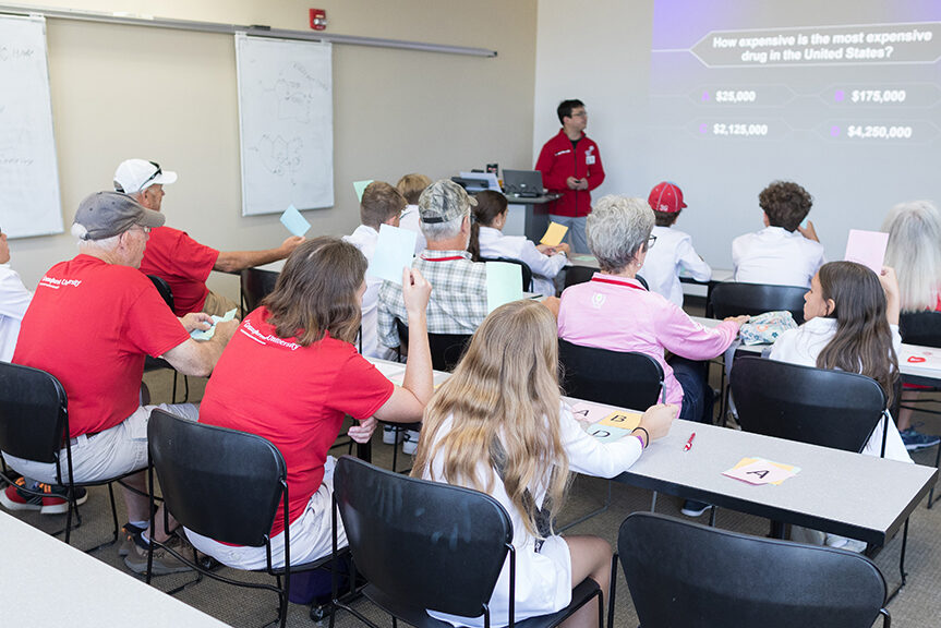 Tables of attendees look toward a projection screen bearing a multiple choice question