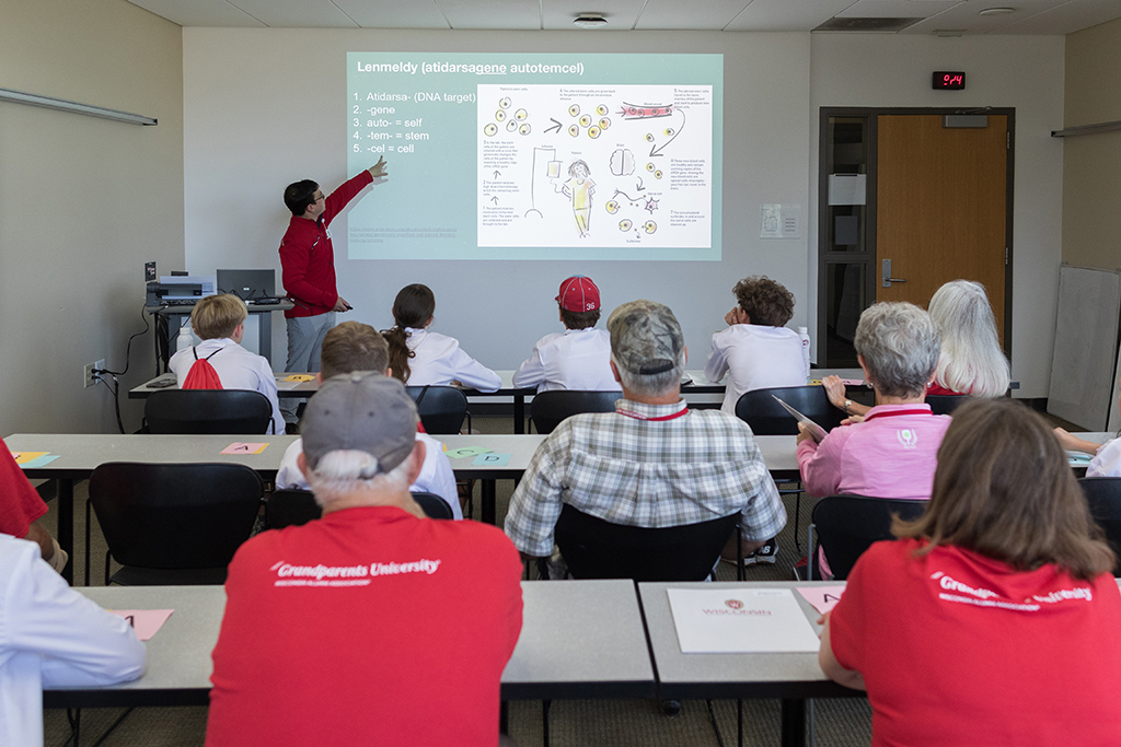 Tables of attendees look toward a student who is explaining lenmeldy (atidarsagene autotemcel)