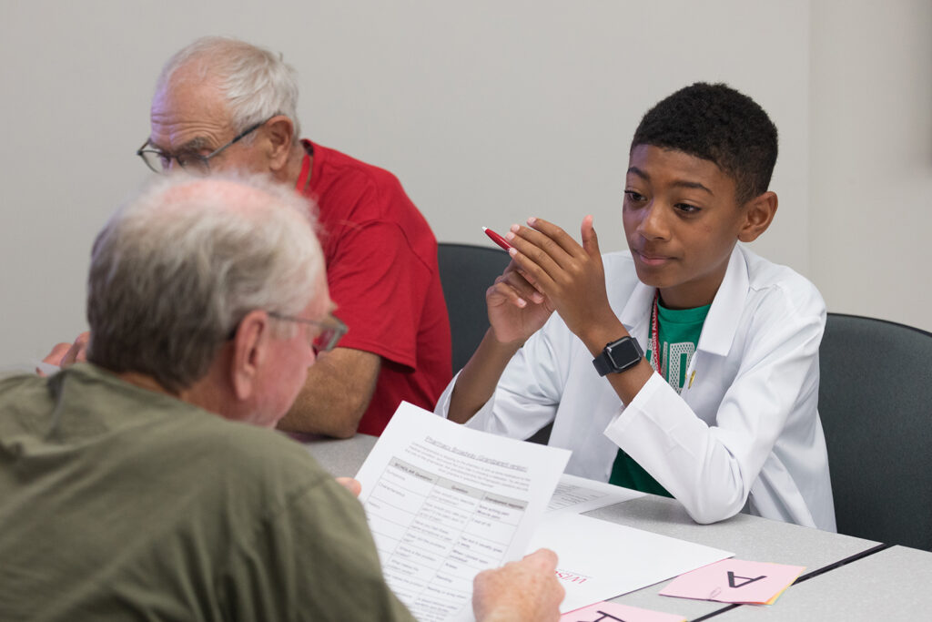 A young boy smiles and looks on as an older attendee reviews a worksheet