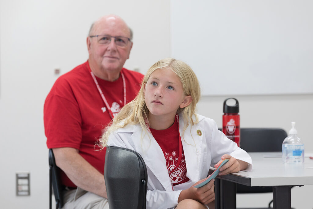 A young attendee with an older attendee, listening to a presenter