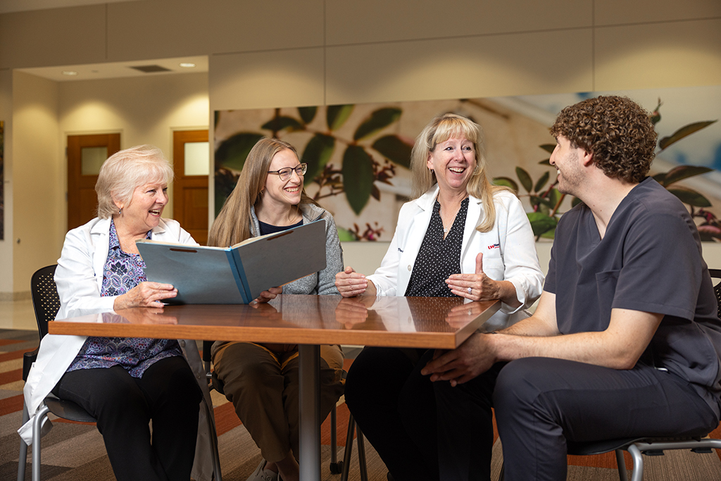 Sara Lentz, Susan Johnston, and two pharmacy residents sit together at a table and speak while smiling