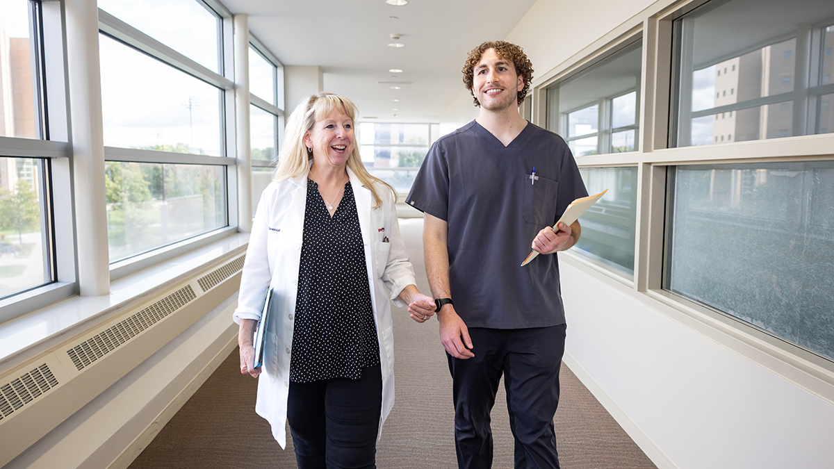 Susan Johnston in a white coat and Blake O'Connor in scrubs walk through a hallway
