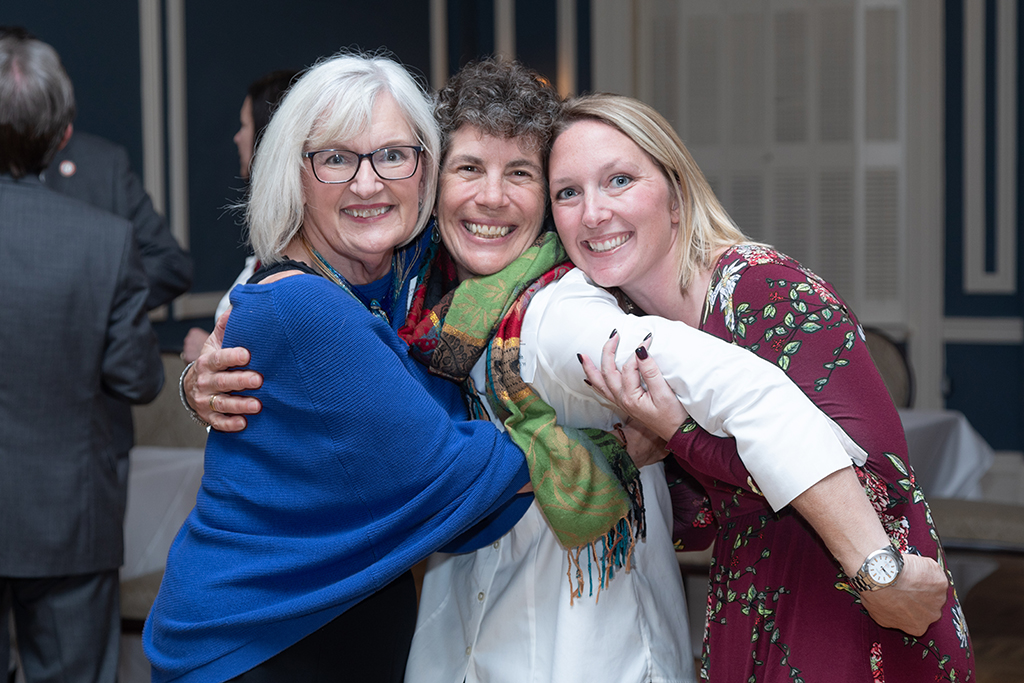 Bonnie Fingerhut, Susan Stein, and another woman hug and smile at the camera.