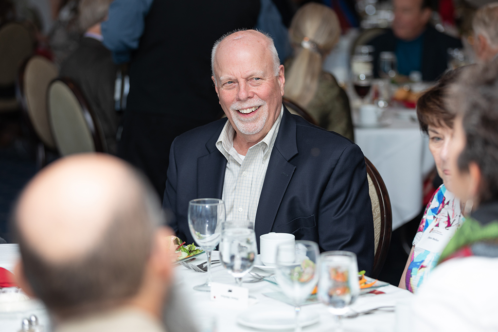 Bill Mellon smiles while seated for dinner.
