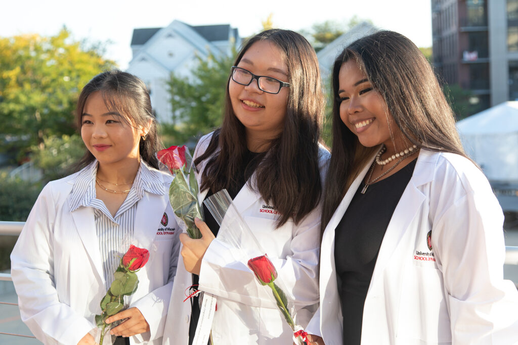 Pharm students together holding roses and wearing their white coats after white coat ceremony