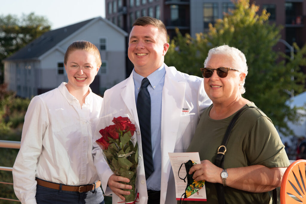 Student holding roses and wearing their white coat with their family after white coat ceremony