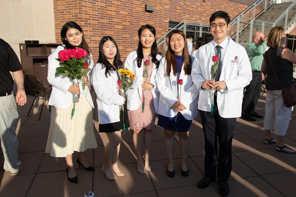 Pharm students holding roses and wearing their white coats together after white coat ceremony